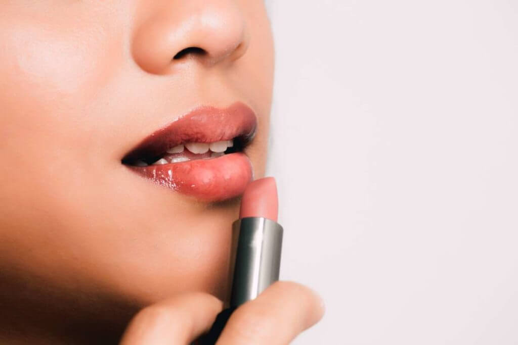 Chica aplicando labial de los productos de maquillaje profesional