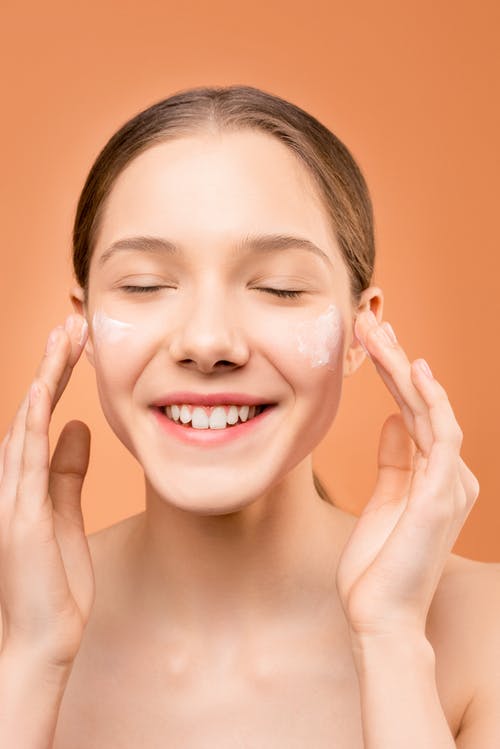 Chica aplicando crema en sus mejillas, preparación de la piel antes del maquillaje