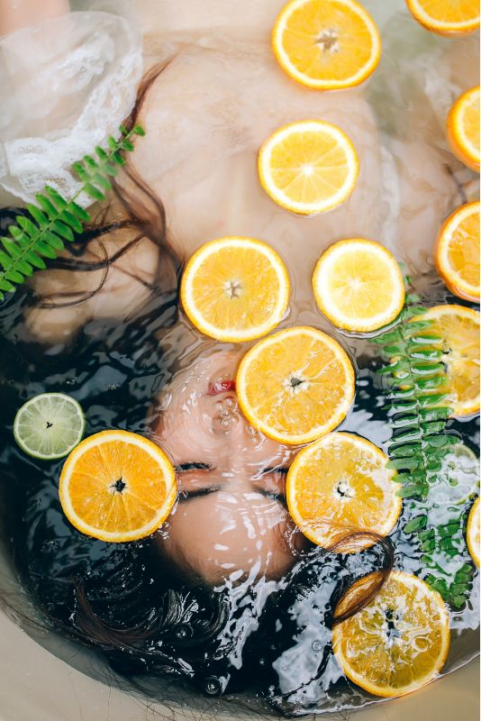 Chica debajo del agua con rodajas de naranja flotando, limpieza facial