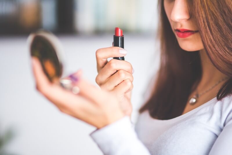 Chica sosteniendo labial y espejo compacto para pintarse los labios, maquillaje navideño